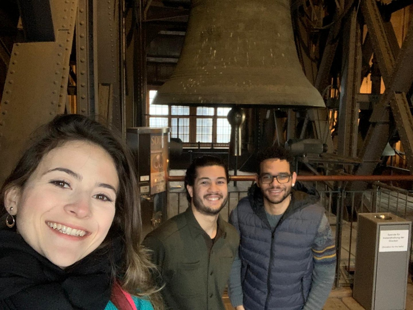 One female student and two mal students in front of the big bell in the cologne cathedral 