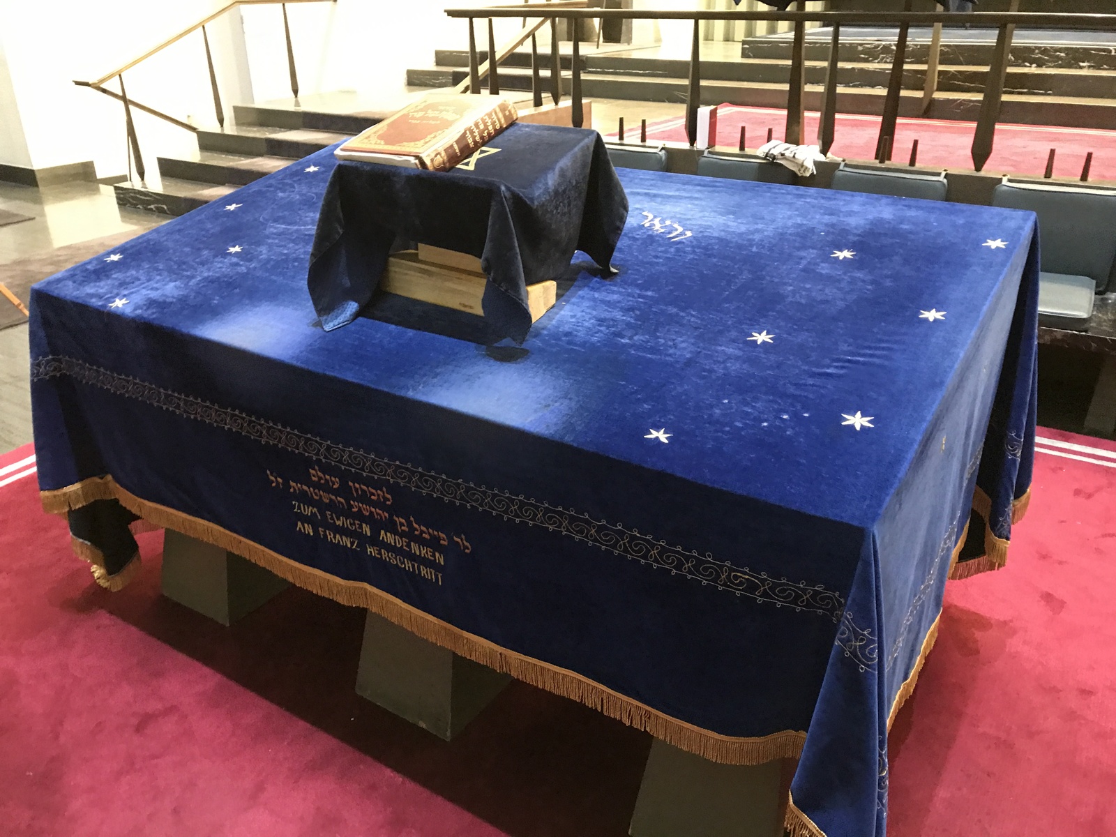 Big table with a blue velvet cloth and on top smaller stand with a book (synagogue).