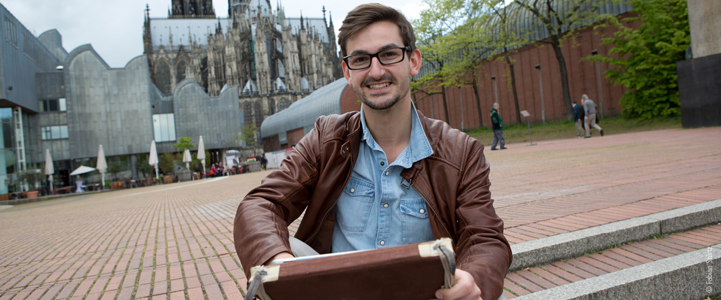 Man sitting on steps with Museum Ludwig and Cologne Cathedral in the background