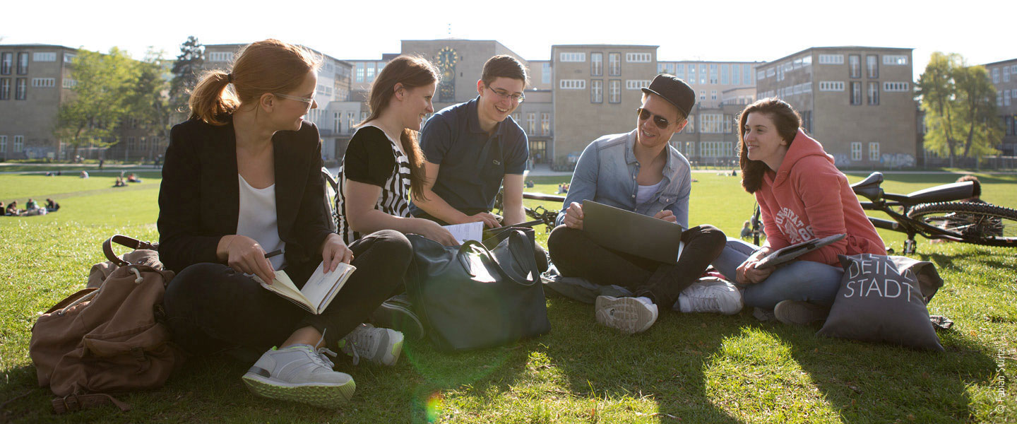 Gruppe Studierender im Park an der Rückseite des Uni Köln Hauptgebäudes im Sonnenschein